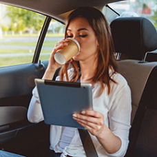 A female traveler inside the car with coffee and ipad using airport transfer